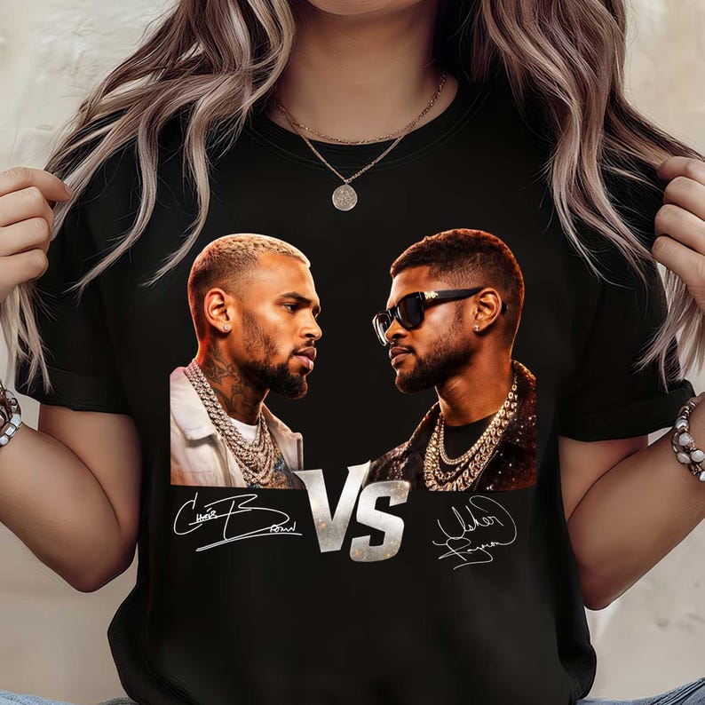 May include: Black t-shirt featuring a graphic of two men facing each other, with the word "VS" in the middle. The shirt includes the signatures of the men below their images. The men are wearing jewelry.