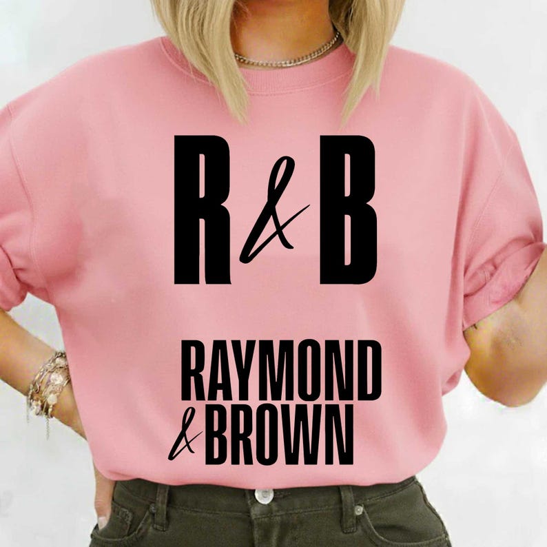 May include: A light pink t-shirt with the text "R & B" in large black letters at the top, and "RAYMOND & BROWN" in black letters below. The shirt has short sleeves.