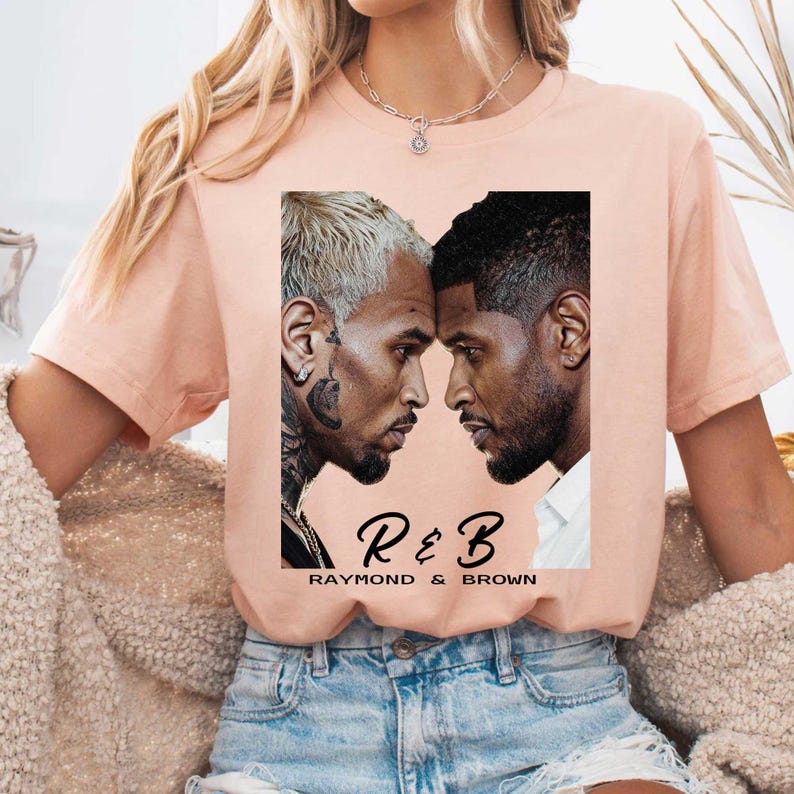 May include: A peach-colored t-shirt featuring a graphic of two men facing each other. The graphic includes the text "R & B" above "Raymond & Brown" in a stylized font. The shirt is worn by a person.