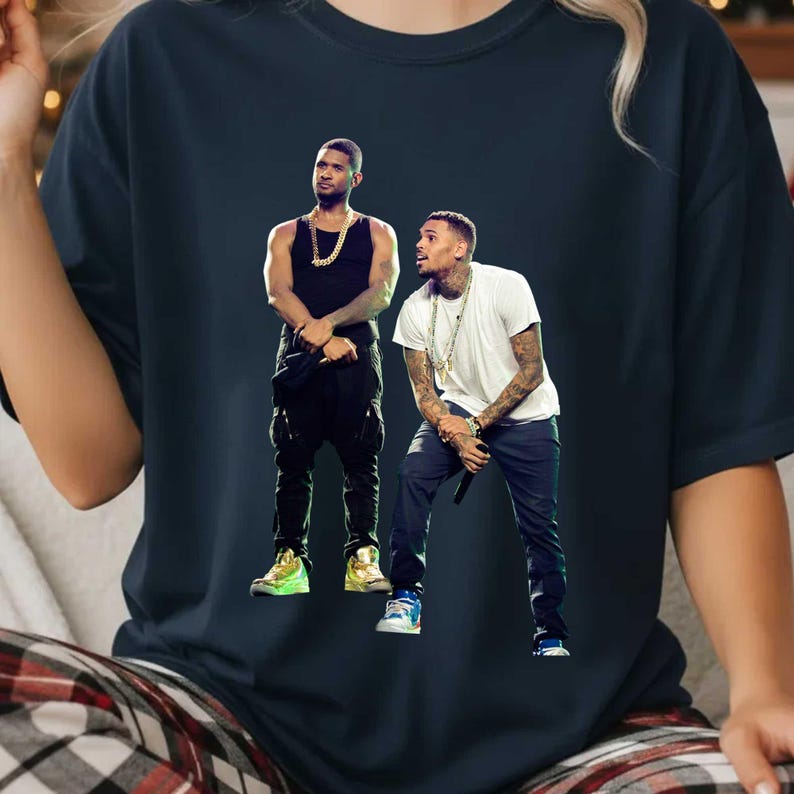 May include: Navy blue t-shirt featuring a graphic of two male musicians. One is wearing a black tank top and the other a white t-shirt. Both are wearing gold chains and jewelry. The image is a vibrant, colorful design.