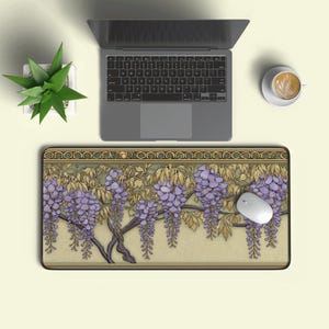 Puede incluir: Alfombrilla de ratón rectangular con un diseño floral de flores de glicina moradas y hojas verdes. La alfombrilla está sobre un fondo beige claro, con un portátil, un ratón y una taza de café visibles.