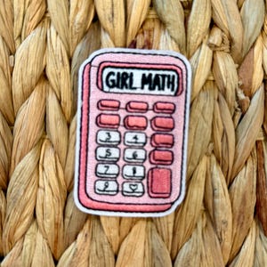 May include: A pink calculator patch with the words "GIRL MATH" in black. The calculator has pink buttons and a pink border. The patch is on a woven, light brown background.