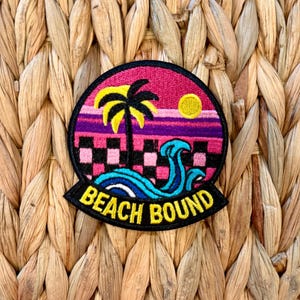 May include: Embroidered patch with a beach scene featuring a palm tree, sunset, and ocean waves. The patch has a black border with the words "BEACH BOUND" in yellow. The background is a woven texture.
