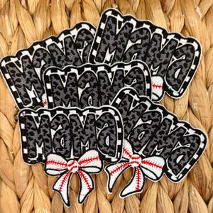 May include: Embroidered patches featuring the word "Mama" in a black and white leopard print. Each patch has a white, checkered border and a red and white baseball-style bow, suitable for clothing or accessories.