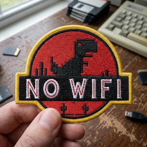 May include: Embroidered patch with a red and black design featuring a pixelated dinosaur silhouette and the words "NO WIFI." The patch has a yellow border and is held against a wooden surface.