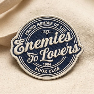 May include: Embroidered patch with the text "Proud Member of the Enemies to Lovers Book Club 1984." The patch is navy blue with white lettering and border. The patch is circular with a unique shape.
