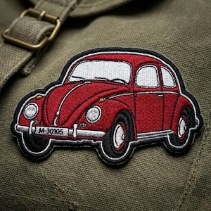 May include: A red embroidered patch in the shape of a classic car, featuring white windows, black tires, and a white license plate with the number M-30105. The patch has a black border and is set against a green fabric background.