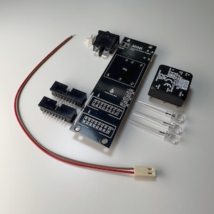 Könnte beinhalten: Eine schwarze Leiterplatte mit der Aufschrift MINI Eurorack Power Supply, zwei schwarzen Stiftleisten, einem schwarzen Netzteilmodul, einem schwarzen Wippschalter, drei klaren LEDs und einem rot-braunen Kabel mit weißem Stecker.