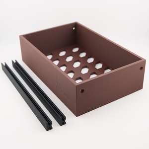 Pode incluir: Uma caixa de armazenamento retangular marrom com uma base em favo de mel e dois trilhos pretos. A caixa tem um logotipo na lateral e é projetada para organizar itens. A caixa é feita de um material sólido.