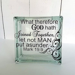May include: A square, clear glass block featuring black vinyl lettering that reads: What therefore GOD hath joined together, let not MAN put asunder Mark 19:9. The text is accompanied by a black decorative swirl design on the right side.