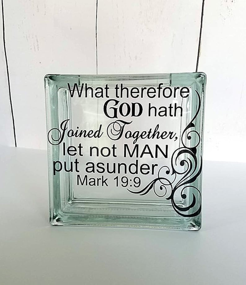 May include: A square, clear glass block featuring black vinyl lettering that reads: What therefore GOD hath joined together, let not MAN put asunder Mark 19:9. The text is accompanied by a black decorative swirl design on the right side.