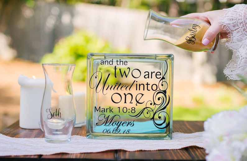 Personalized wedding sand ceremony set consisting of glass block and 2 glass vases. Bride is pouring sand as would happen in ceremony to intermix the sand like the joining of two lives in marriage.