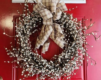 Corona de vid de bayas artificiales color marfil con lazo a cuadros neutros para decorar la puerta principal.