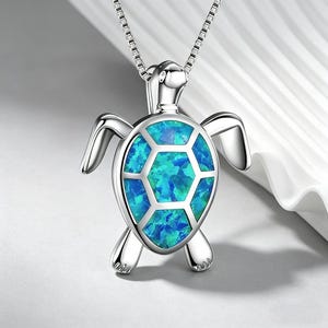 May include: A silver-toned turtle pendant necklace featuring a shell inlaid with iridescent blue and green opal-like segments. The turtle has a polished metallic head, four flippers, and is suspended from a delicate silver-toned box chain.
