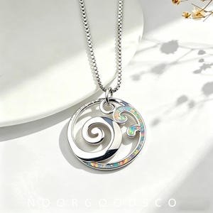 May include: A silver-toned necklace featuring a circular pendant with a polished metal spiral design and a curved wave-shaped inlay of iridescent, multi-colored opal-like material. The pendant hangs from a delicate silver-toned box chain.