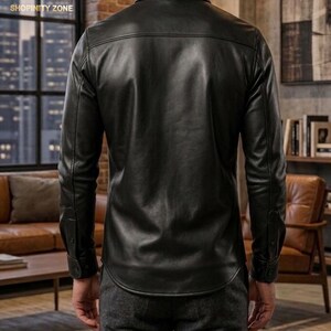 May include: A black leather shirt with long sleeves and buttoned cuffs. The shirt has a classic collar and a curved hemline. The back of the shirt is visible, showcasing the smooth texture of the leather. The shirt is worn with gray pants.