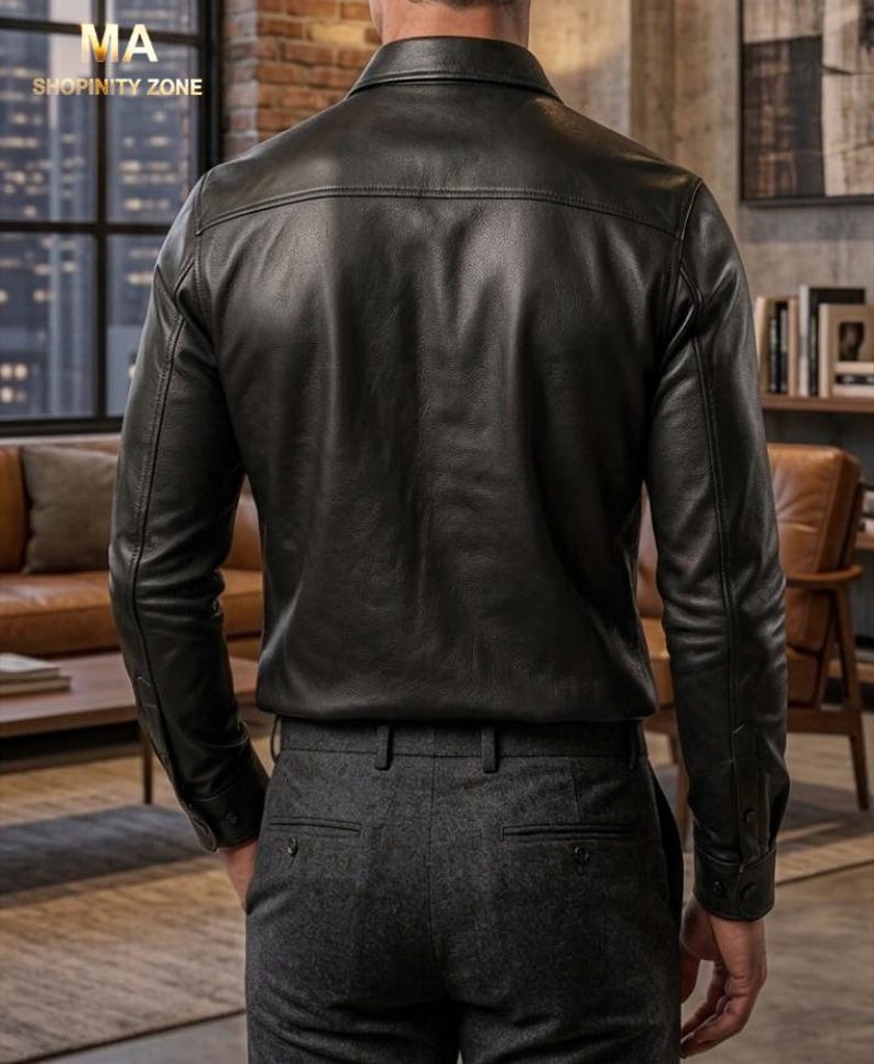 May include: A black leather shirt with long sleeves and buttoned cuffs. The shirt has a classic collar and a tailored fit. The model is wearing gray dress pants. The image is taken from the back, showcasing the shirt's design and texture.