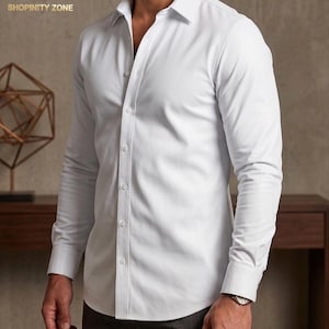 May include: A white button-down shirt with long sleeves. The shirt has a classic collar and is buttoned up the front. The image includes the text "MA SHOPINITY ZONE" in the upper left corner.
