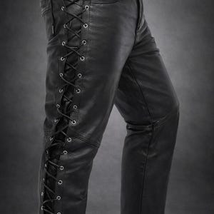 Könnte beinhalten: Schwarze Lederhose mit seitlicher Schnürung, schwarzen Ösen und schwarzer Kordel, die von der Taille bis zum Saum verläuft. Die Hose verfügt über eine Standardtasche an der Hüfte und eine horizontale Naht über dem Knie. Text lautet MA SHOPINITY ZONE.