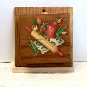 May include: Wooden kitchen-themed wall art featuring a rolling pin, measuring cup, and muffin tin. The art includes painted tulips in red, orange, and green. The rolling pin is approximately 10 inches long.