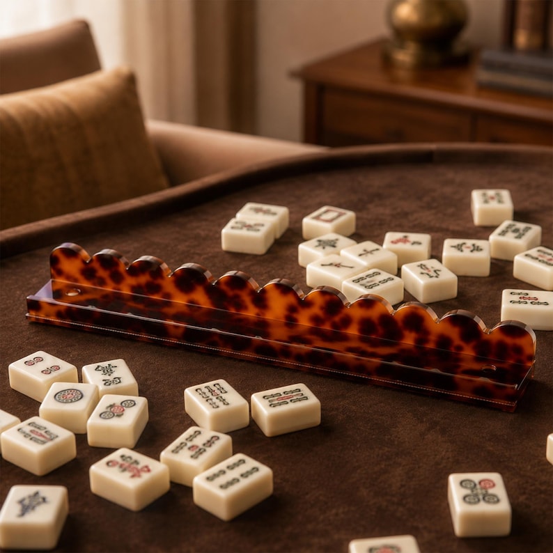 May include: A close-up shot of a brown and tan mahjong set. The set includes ivory-colored tiles with various symbols and a tortoise-shell-patterned tile rack. The tiles are scattered on a brown surface.