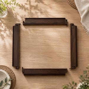 May include: Four dark brown wooden frame pieces arranged on a light brown wooden surface. The pieces are rectangular with a grooved design. The arrangement suggests a picture frame or a similar structure. The wood grain is visible.