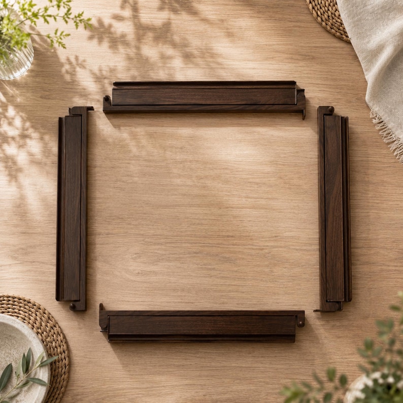 May include: Four dark brown wooden frame pieces arranged on a light brown wooden surface. The pieces are rectangular with a grooved design. The arrangement suggests a picture frame or a similar structure. The wood grain is visible.