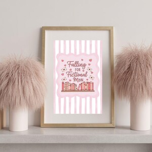 Puede incluir: Una impresión enmarcada con el texto "Falling for Fictional Men" en un diseño rosa y blanco. La impresión está en un marco dorado y está flanqueada por dos piezas decorativas rosas y esponjosas en jarrones blancos. El tema es el romance y los libros.