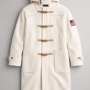 May include: Cream-coloured duffel coat with a hood and wooden toggles. Features two front pockets, buttoned cuffs, and an American flag patch on the upper left sleeve. A classic winter coat.