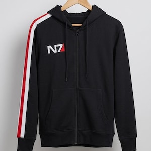 Pode incluir: Moletom preto com zíper e uma faixa branca e vermelha na manga esquerda. O moletom apresenta as letras "N7" em branco no peito. O moletom está pendurado em um cabide de madeira.