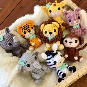 May include: A collection of handmade crochet animal toys, including a giraffe, lion, tiger, zebra, elephant, rhino, monkey, and hippo. Each toy is a different color and has a cute, friendly design. They are arranged in a woven basket.