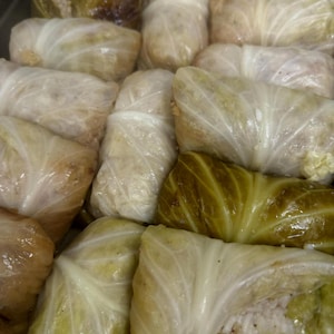 Könnte beinhalten: Nahaufnahme eines Tabletts mit gefüllten Kohlrouladen. Die Rollen sind in hellgrüne Kohlblätter gewickelt und mit einer hellen Füllung gefüllt. Einige Blätter haben einen dunkleren Grünton.