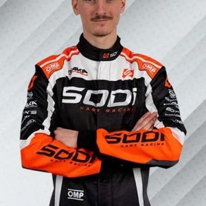 K&ouml;nnte beinhalten: Ein Rennanzug in Schwarz, Wei&szlig; und Orange mit der Aufschrift "SODI KART RACING" und "OMP". Der Anzug hat einen schwarzen Kragen und Akzente. Der Hintergrund ist ein Farbverlauf aus Wei&szlig; und Grau.