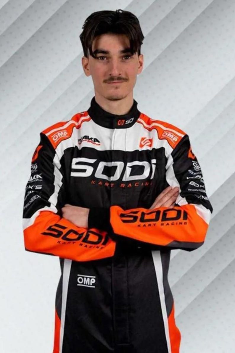 K&ouml;nnte beinhalten: Ein Rennanzug in Schwarz, Wei&szlig; und Orange mit der Aufschrift "SODI KART RACING" und "OMP". Der Anzug hat einen schwarzen Kragen und Akzente. Der Hintergrund ist ein Farbverlauf aus Wei&szlig; und Grau.