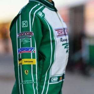 May include: Green and white racing suit with sponsor logos such as "TONY KARI Racing Team" and "VORTEX". The suit has white vertical stripes and the "Ferrari Driver Academy" logo. The OMP logo is visible.