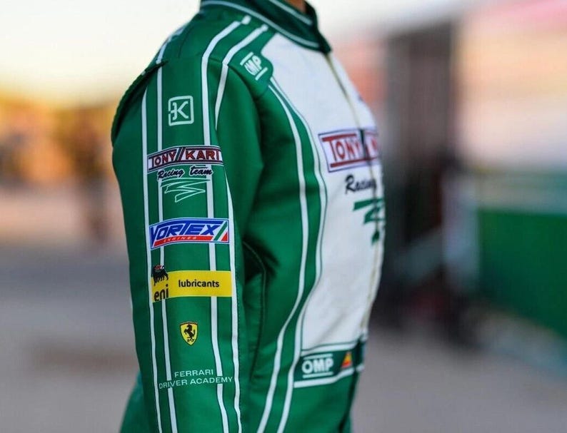 May include: Green and white racing suit with sponsor logos such as "TONY KARI Racing Team" and "VORTEX". The suit has white vertical stripes and the "Ferrari Driver Academy" logo. The OMP logo is visible.