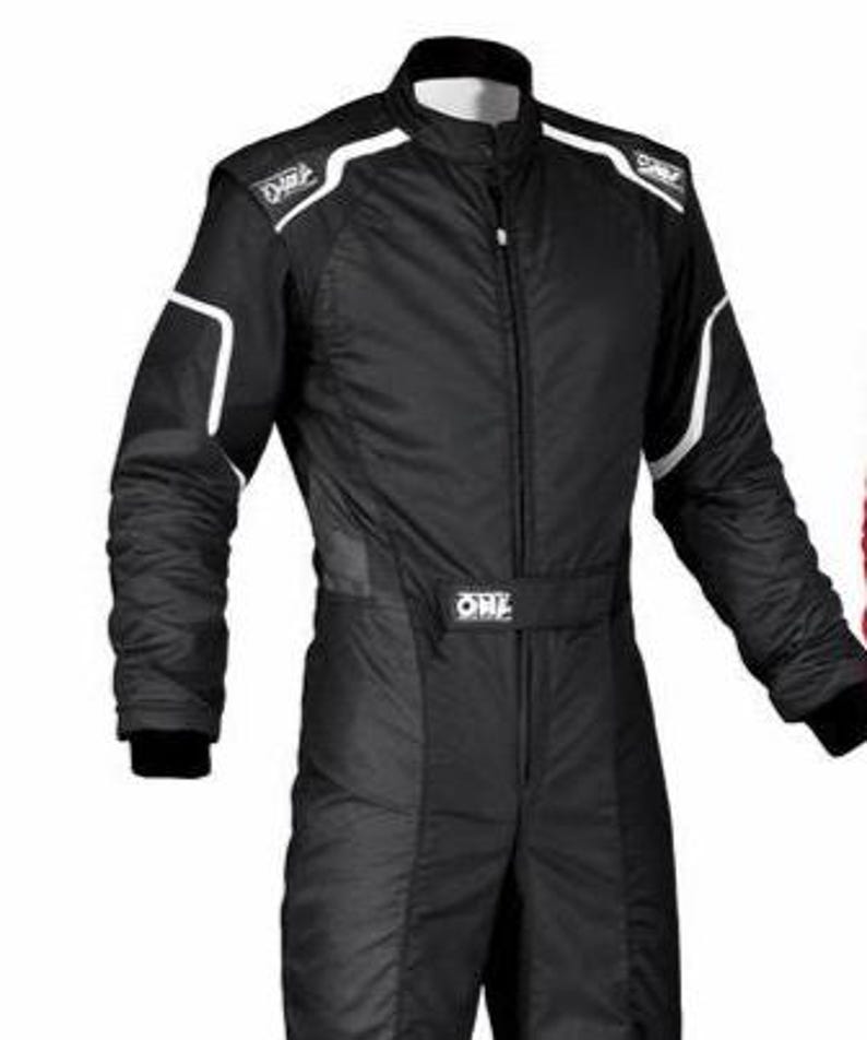 May include: A black racing suit featuring a high collar, a central zipper closure, and white piping accents along the shoulders and sleeves. The garment displays the OMP brand logo on the shoulder epaulets and a central waist belt.