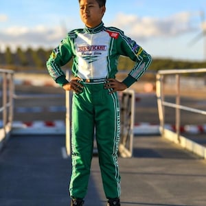May include: A person in a green and white racing suit with the text "TONY KART Racing Team". The suit has white stripes and accents. The person is standing on a racetrack.