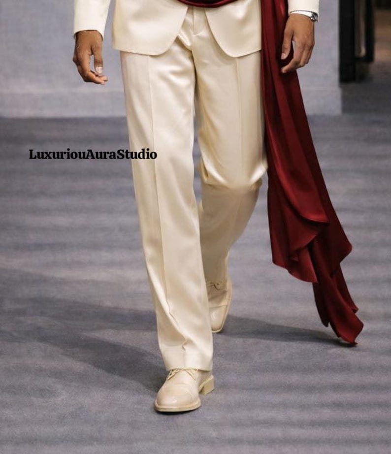 May include: Cream-colored suit with matching shoes. A flowing burgundy sash adds a pop of color. The text "LuxuriousAuraStudio" is visible. The suit appears to be made of a satin-like material, suggesting a formal or special occasion outfit.