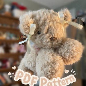 Op de afbeelding: Een beige pluche teddybeer met warrige vacht, donkere ogen en een geborduurde neus. De beer heeft twee crèmekleurige satijnen linten om de oren gestrikt. De tekst "PDF Pattern" staat in witte letters met een lichtbruine omlijning.