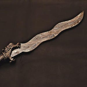 Op de afbeelding: Een sierlijke dolk met een golvend lemmet en een handvat met drakenmotief. Het lemmet heeft een uniek, patroonontwerp. Het handvat heeft ingewikkelde gravures en een drakenkop aan de basis van het lemmet. De dolk is van metaal en staat tegen een donkere achtergrond.