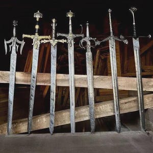 Könnte beinhalten: Eine Ansammlung von sechs verzierten Schwertern mit detaillierten Griffen und Klingen. Die Schwerter werden vor einem hölzernen Hintergrund präsentiert, der ihre komplizierten Designs und ihre Handwerkskunst zeigt. Die Klingen haben ein strukturiertes Muster.