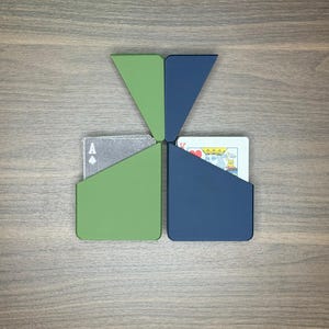 May include: A unique playing card holder in a geometric design. The holder is composed of four triangular sections in green and blue, with playing cards visible in two of the sections. The Ace of Spades and the King of Hearts are visible.