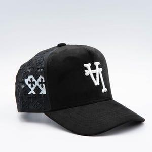 May include: Black baseball cap with white embroidered logo on the front and decorative floral pattern on the side. The cap features a curved brim and a button on top. The logo appears to be the letters "LA" in a stylized font.