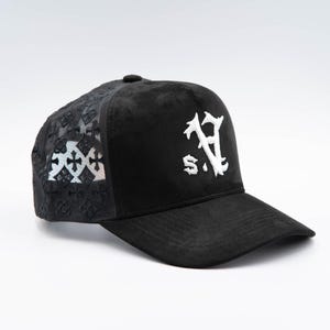 May include: A black baseball cap featuring a white embroidered logo with the letters S.V. on the front panel. The side and back panels are constructed from a black mesh material decorated with a repeating pattern of small black cross symbols.
