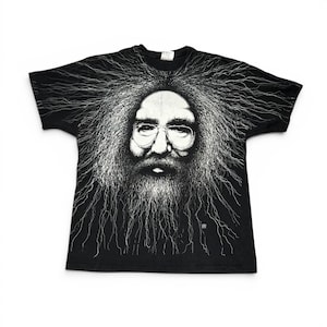 May include: Black t-shirt featuring a detailed white illustration of a man with glasses, a long beard, and flowing hair. The graphic is centered on the shirt, creating a striking contrast against the dark fabric. The design has a vintage, artistic feel.