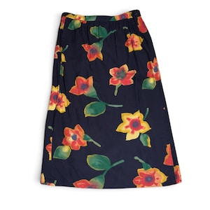 May include: A dark navy blue midi skirt featuring a repeating watercolor-style floral print. The pattern consists of vibrant red, orange, and yellow flowers with green leaves scattered across the fabric. The skirt has a straight cut and a waistband.