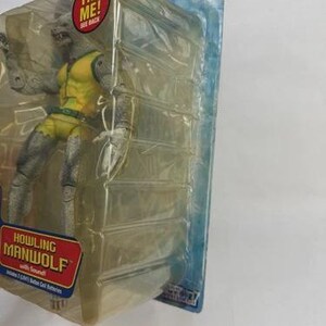 May include: A Howling Manwolf action figure from The Amazing Spider-Man series, packaged in a clear plastic case. The figure is gray and yellow, with the text "TRY ME!" and "HOWLING MANWOLF" on the packaging.