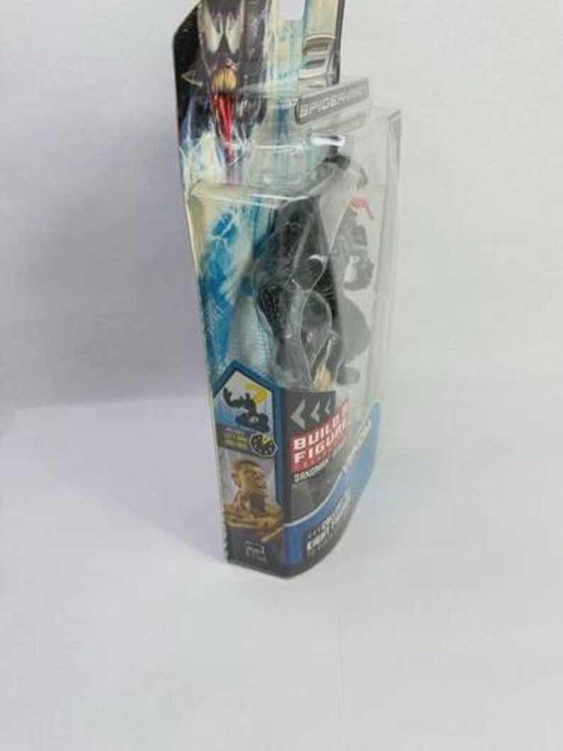 May include: A black Venom action figure in a clear plastic package. The packaging features a blue and white design with the words "Build Figure" and "Venom" printed on it. The figure is a collectible item.