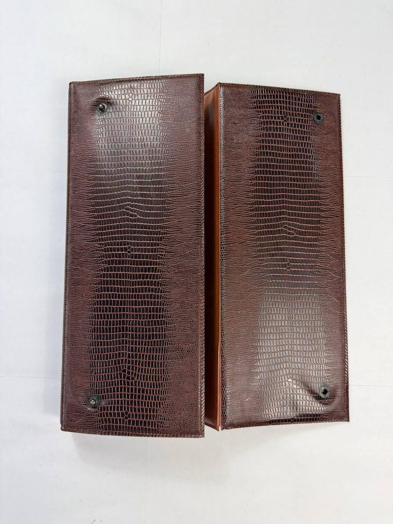 May include: Two brown, rectangular leather-like cases with a reptile skin texture. Each case has a dark brown exterior and a lighter brown interior. The cases are secured with a single, dark-colored button on each. The cases are open, revealing the interior.